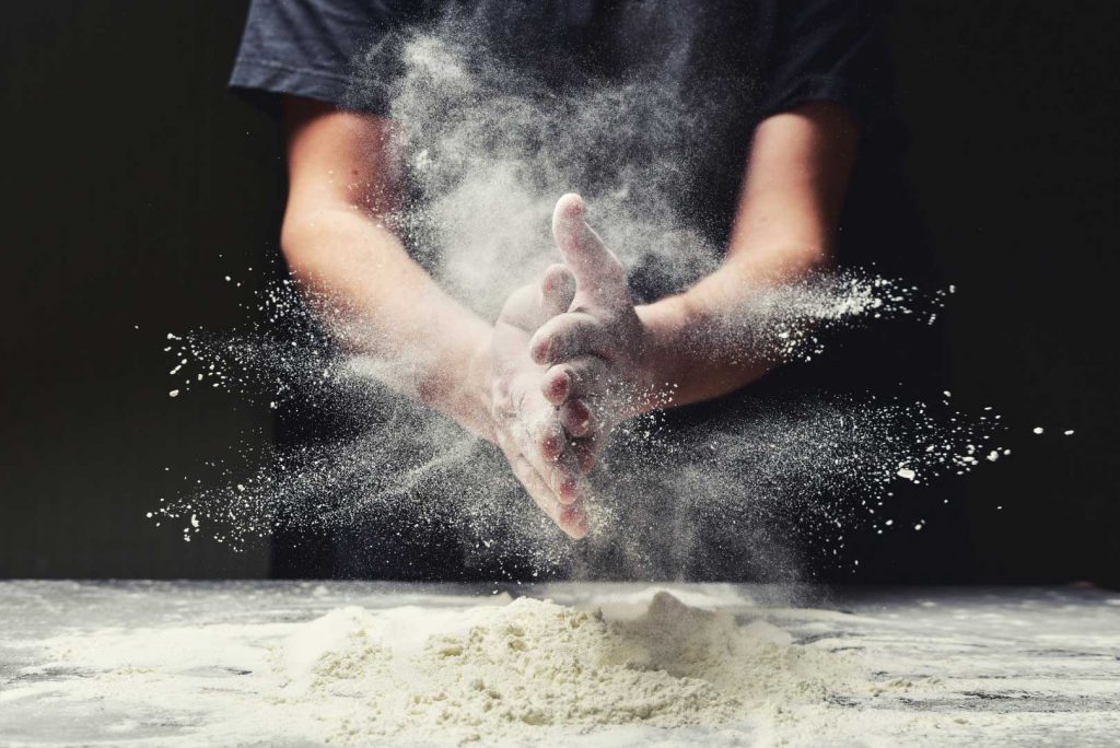 Un panettiere al lavoro picchia i palmi e crea una nuvola di farina